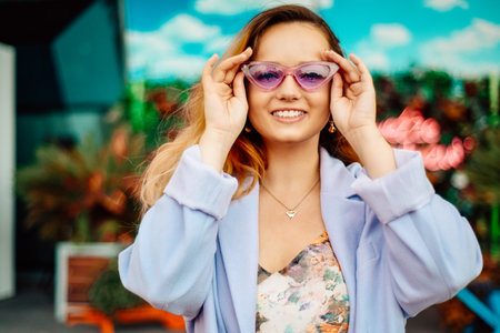 A girl in a dress, jacket and purple sunglasses poses at the festival portrait. Smile and joy, emotions.の写真素材