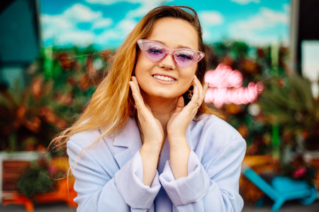 A girl in a dress, jacket and purple sunglasses poses at the festival portrait. Smile and joy, emotions.の写真素材
