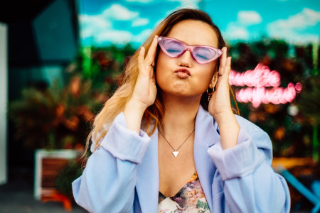 A girl in a dress, jacket and purple sunglasses poses at the festival. Woman blow kiss to cameraの写真素材