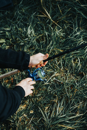 Male hands hold a fishing rod against the background of grass. Fishingの写真素材