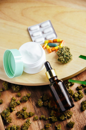 Marijuana cbd and thc. Marijuana buds are on the table. Glass bottle for oil, cosmetics with pipette. Cream and cosmetics with marijuana, pills, medicine and treatmentの写真素材