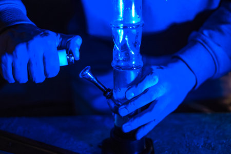 Male hands clog a bong with marijuana. A man smokes weed through a bong. Neon blue light. CBD treatment. medicine and drugsの写真素材