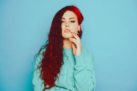 Woman in a blue sweater on a blue background posing. A beautiful brunette with long hair and tunnels in her ears. Eyeliner and trendy makeupの写真素材