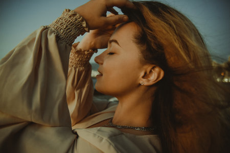 Girl on the beach with long hair, summer mood. Sunset, woman in a beautiful dress on vacation, and accessories, portrait, wind in her hairの写真素材