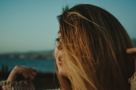 Girl on the beach with long hair, summer mood. Sunset, woman in a beautiful dress on vacation, and accessories, portrait, wind in her hairの写真素材