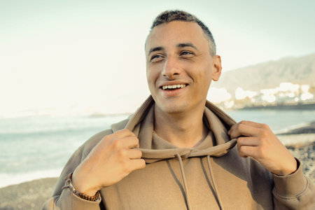 A man in a beige hoodie against the background of the sea. A guy is walking on the beach and...