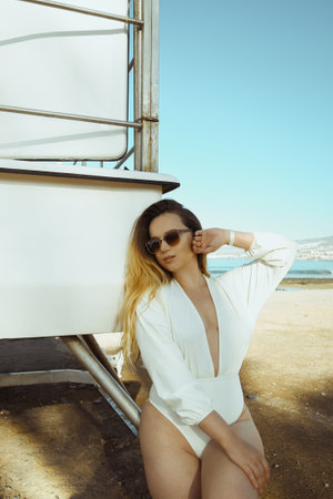 Beautiful bohemian styled and tanned girl , tropical beach in sunlight. Beautiful young woman standing at sea beach in sensual white swimsuit and sun glasses.の写真素材