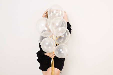 Gorgeous woman with balloons in black dress and corset with jewelry, long wavy hair posing on white background. Fashion , all black style.の写真素材