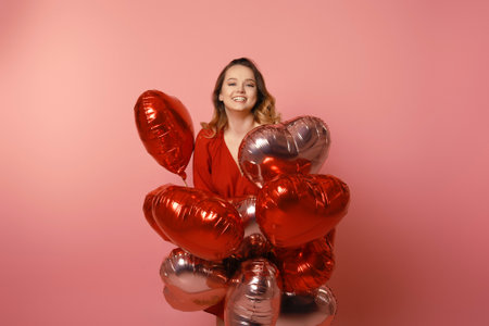 Valentine's Day Beauty girl with red dress and pink air balloons. Happy young woman posing and laughing at the camera. Loveの写真素材