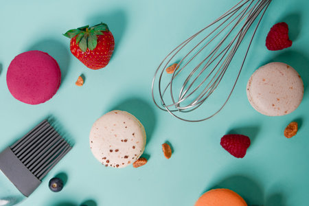 colorful macarons. Small French cakes. Cooking, whisk, broken macarons, fruits, strawberries, raspberries and blackberries. Cooking process on a blue background, whisk, strawberries.の写真素材
