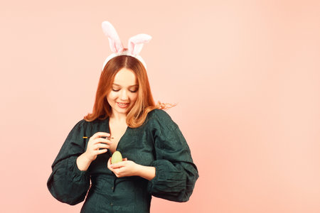 A girl in a green dress celebrates Easter and paints eggs. Holiday Easter eggs and smile, holiday bunny ears on pretty womanの写真素材