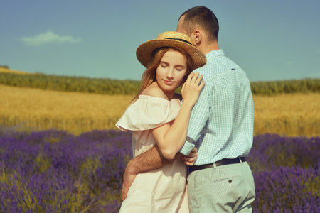 A couple in love in a field of lavender at sunset in good weather. Beautiful woman in a dress and straw panama with a man on the background of nature, love and feelings. Blue, purple lavenderの写真素材