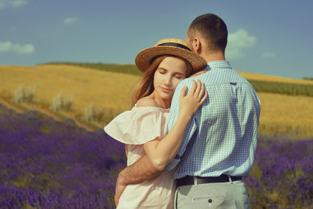 A couple in love in a field of lavender at sunset in good weather. Beautiful woman in a dress and straw panama with a man on the background of nature, love and feelings. Blue, purple lavenderの写真素材