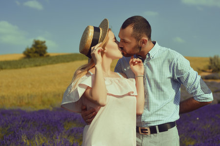 Couple in love kissing in a lavender field. Romance and travel, love. A pretty girl in a dress and a straw hat, and a man.の写真素材