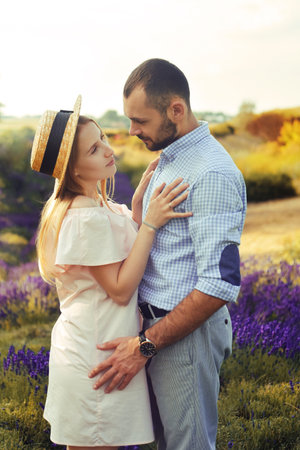 A couple in love in a field of lavender at sunset in good weather. Beautiful woman in a dress and straw panama with a man on the background of nature, love and feelings. Blue, purple lavenderの写真素材