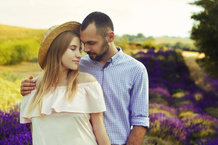 A couple is standing in a lavender field. The blonde in a pink dress and with a straw hat, against the background of a purple field of flowers. Romance in relationships, aromasの写真素材