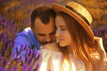 A couple in love in a field of lavender at sunset in good weather. Beautiful woman in a dress and straw panama with a man on the background of nature, love and feelings. Blue, purple lavenderの写真素材