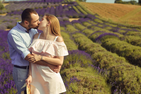 A couple in love in a field of lavender at sunset in good weather. Beautiful woman in a dress and straw panama with a man on the background of nature, love and feelings. Blue, purple lavenderの写真素材
