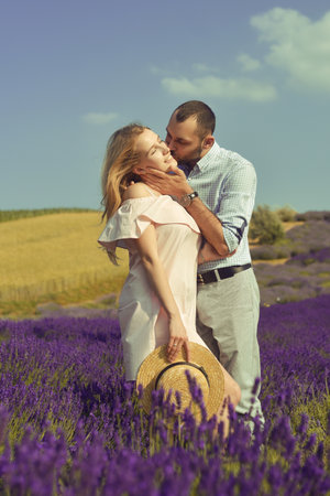 A couple in love in a field of lavender at sunset in good weather. Beautiful woman in a dress and straw panama with a man on the background of nature, love and feelings. Blue, purple lavenderの写真素材
