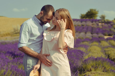 A couple in love in a field of lavender at sunset in good weather. Beautiful woman in a dress and straw panama with a man on the background of nature, love and feelings. Blue, purple lavenderの写真素材