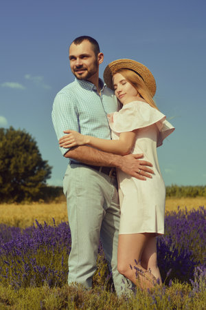 A couple in love in a field of lavender at sunset in good weather. Beautiful woman in a dress and straw panama with a man on the background of nature, love and feelings. Blue, purple lavenderの写真素材