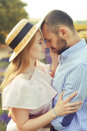A couple in love in a field of lavender at sunset in good weather. Beautiful woman in a dress and straw panama with a man on the background of nature, love and feelings. Blue, purple lavenderの写真素材