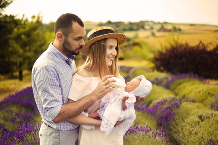 Happy caucasian family mother, father and daughter are wearing white clothes are having fun in lavender field. A couple is feeding a baby from a bottle, baby milk. Love, young coupleの写真素材