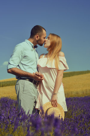 A couple in love in a field of lavender at sunset in good weather. Beautiful woman in a dress and straw panama with a man on the background of nature, love and feelings. Blue, purple lavenderの写真素材