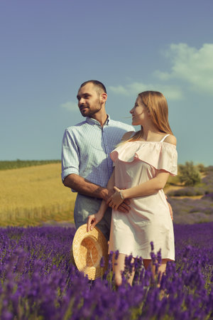 A couple in love in a field of lavender at sunset in good weather. Beautiful woman in a dress and straw panama with a man on the background of nature, love and feelings. Blue, purple lavenderの写真素材