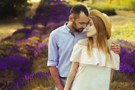 A couple is standing in a lavender field. The blonde in a pink dress and with a straw hat, against the background of a purple field of flowers. Romance in relationships, aromasの写真素材
