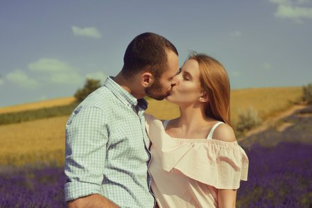 A couple in love in a field of lavender at sunset in good weather. Beautiful woman in a dress and straw panama with a man on the background of nature, love and feelings. Blue, purple lavenderの写真素材