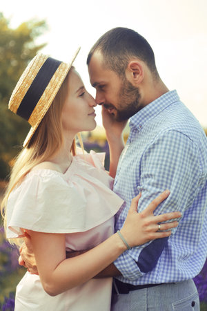 A couple in love in a field of lavender at sunset in good weather. Beautiful woman in a dress and straw panama with a man on the background of nature, love and feelings. Blue, purple lavenderの写真素材