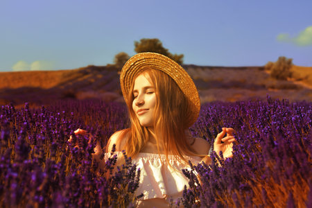 Beautiful girl on the lavender field. Beautiful woman in the lavender field at sunset. soft focus. Provence, France. A girl in pink dress and hat walking trough lavender fields and enjoys natureの写真素材