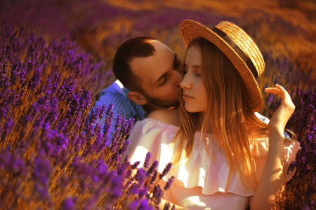 A couple in love in a field of lavender at sunset in good weather. Beautiful woman in a dress and straw panama with a man on the background of nature, love and feelings. Blue, purple lavenderの写真素材