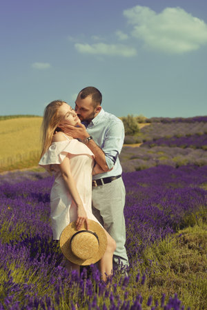 Couple in love kissing in a lavender field. Romance and travel, love. A pretty girl in a dress and a straw hat, and a man.の写真素材