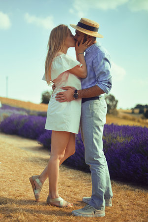 A couple in love in a field of lavender at sunset in good weather. Beautiful woman in a dress and straw panama with a man on the background of nature, love and feelings. Blue, purple lavenderの写真素材