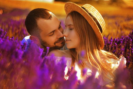 A couple in love in a field of lavender at sunset in good weather. Beautiful woman in a dress and straw panama with a man on the background of nature, love and feelings. Blue, purple lavenderの写真素材