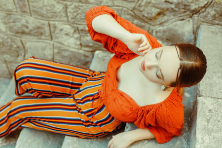 Gorgeous brunette posing lying on the stairs. Jewelry silver earrings, professional makeup, yellow suit. elegant tourist.の写真素材