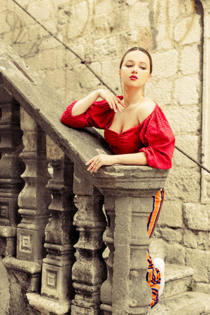 A beautiful girl in red is standing on the old stairs to the castle. Woman in accessories and professional make-up. fashion and styleの写真素材