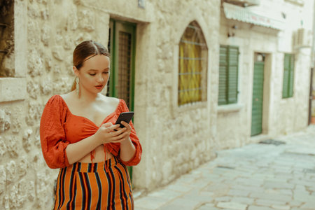 Woman in the old city and posing. Beautiful stylish girl with a smartphone in her hands, online dating, chat. Travel around Europeの写真素材
