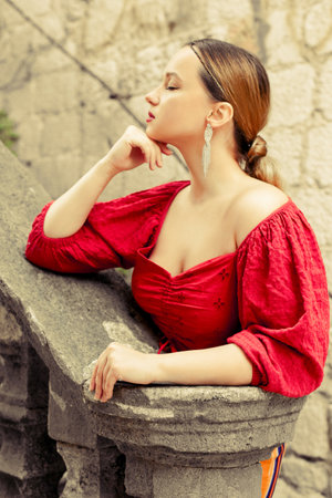 A beautiful girl in red is standing on the old stairs to the castle. Woman in accessories and professional make-up. fashion and styleの写真素材
