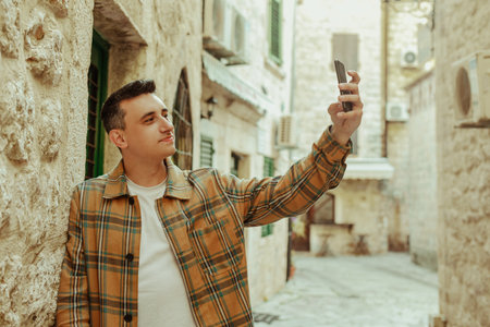Portrait of a guy on the background of the old city with a phone. The guy looks at the smartphone. Communication abroad, roaming, video calls or selfiesの写真素材
