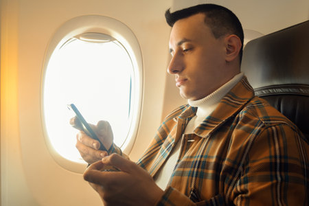 A man in a half-empty plane with a phone. Guy traveler looking at smartphone.の写真素材