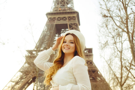An incredibly beautiful girl in a long white dress and a beret against the background of the Eiffel Tower. Fashion in Paris, travel and weddings. Romance in the city of love, a woman smiles.の写真素材
