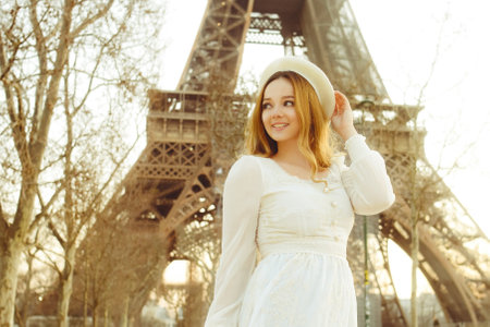 A girl against the backdrop of the Eiffel Tower in Paris in a beret and a dress with curled hair, a romantic journey. Woman laughing and looking awayの写真素材