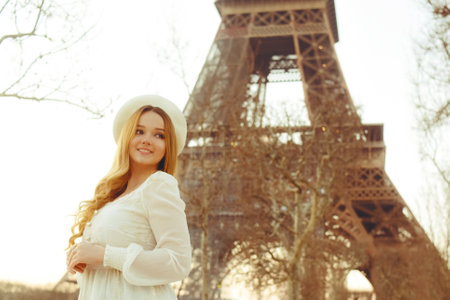Beautiful blonde in Paris with the Eiffel Tower in the background in a beret and white dress. The woman is laughing and smiling, the girl is on a trip to France.の写真素材