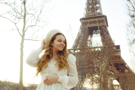Beautiful blonde in Paris with the Eiffel Tower in the background in a beret and white dress. The woman is laughing and smiling, the girl is on a trip to France.の写真素材