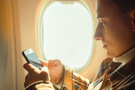 A man in an airplane looks at the phone, Wi-Fi in the airplane cabin. A tourist in a transport in the sky uses a smartphone, plays games, business and entertainment.の写真素材