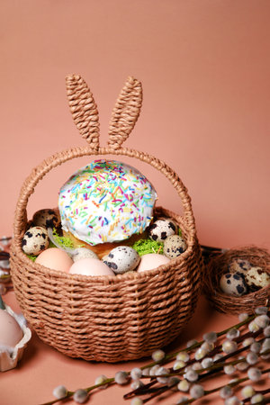 Easter decorations in a basket with rabbit ears. Easter cake and eggs on moss, pussy willow quail eggs and feathers on pink background. Place for text.の写真素材
