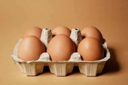 A tray with brown eggs, on a nude background, chicken feathers are flying. Eco products, nutrition, proteins and natural food.の写真素材